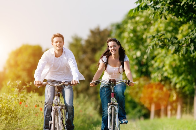 Foto casal feliz, andar de bicicleta ao longo de uma estrada ensolarada