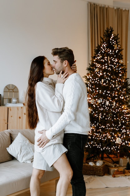 casal feliz apaixonado em uma aconchegante sala de estar branca com enfeites de Natal e uma árvore de Natal