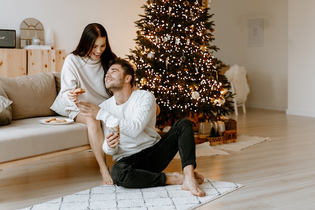 casal feliz apaixonado em uma aconchegante sala de estar branca com enfeites de Natal e uma árvore de Natal