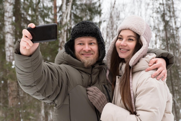 casal feliz apaixonado fazendo seflie andando na floresta de inverno