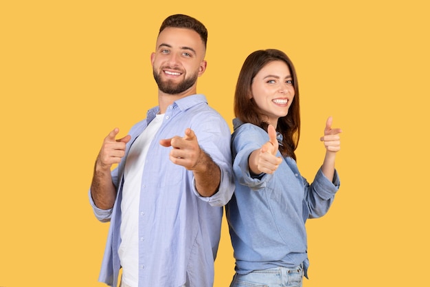 Foto casal feliz apontando para a câmera e sorrindo em roupas casuais