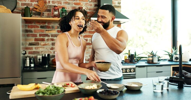 Foto casal feliz bem-estar e degustação em apartamento para nutrição junto com colher para dieta saudável homem mulher e café da manhã com frutas em casa para data de manhã entusiasmado para cozinhar na cozinha