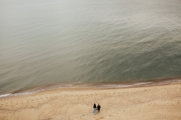 Casal feliz caminhando na praia de longe.