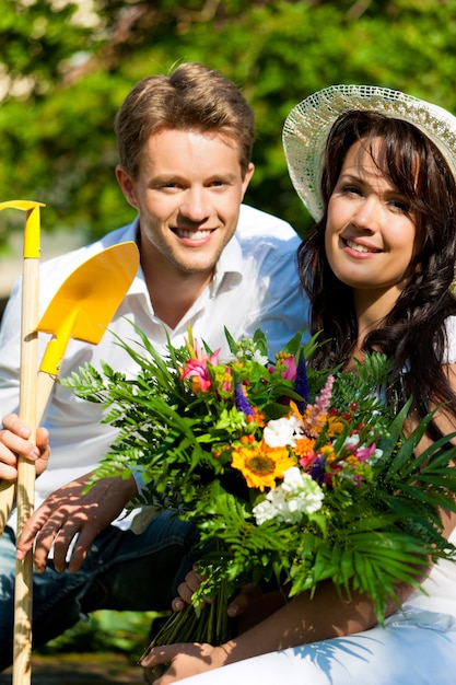 Casal feliz com buquê de flores e ferramentas de jardinagem