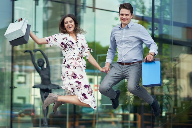 Casal feliz com sacolas de compras depois de fazer compras na cidade, sorrindo e se abraçando.