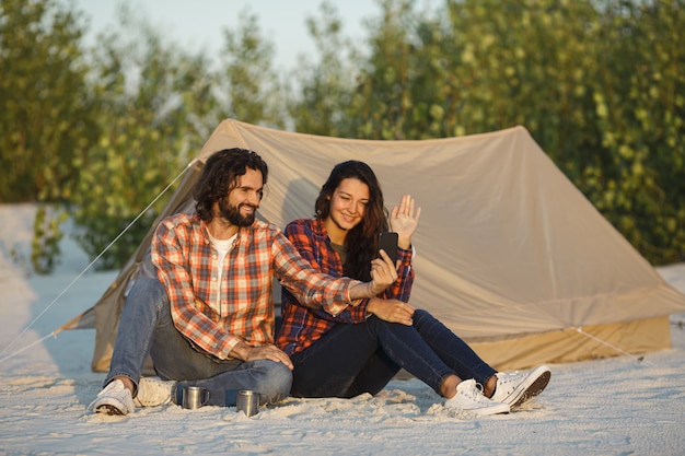 Casal feliz com um smartphone no acampamento perto da barraca ao ar livre