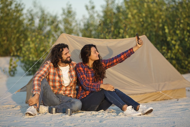 Casal feliz com um smartphone no acampamento perto da tenda ao ar livre