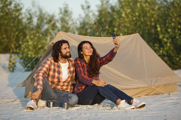 Casal feliz com um Smartphone no acampamento perto da tenda ao ar livre