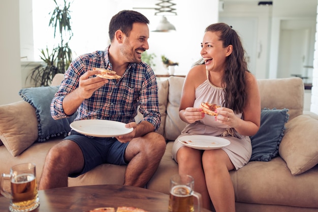 Casal feliz comendo pizza na cama