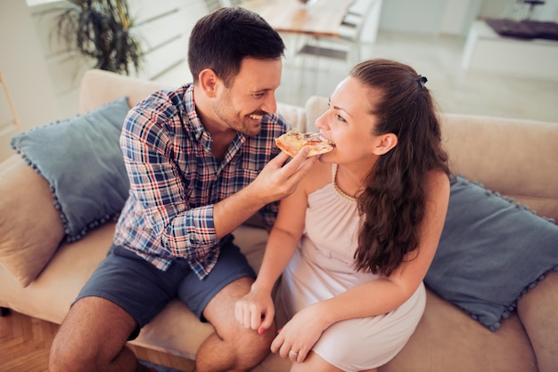 Casal feliz comendo pizza na cama