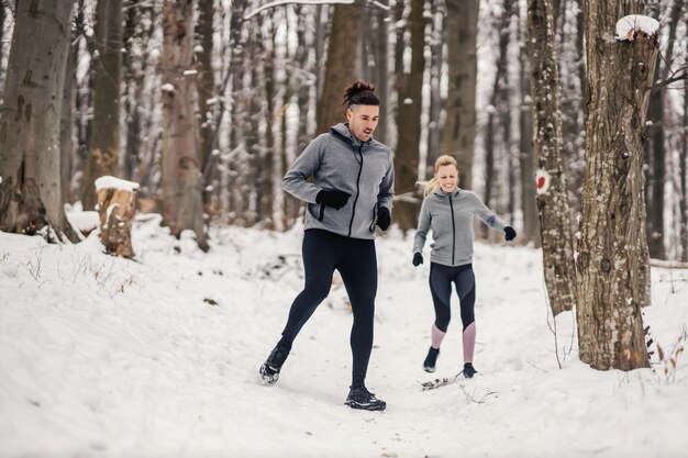 Casal feliz correndo na natureza em um dia de inverno nevado. Diversão, vida saudável, relacionamento