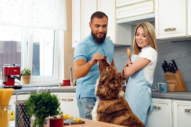 Casal feliz cozinhando comida na cozinha com o cachorro