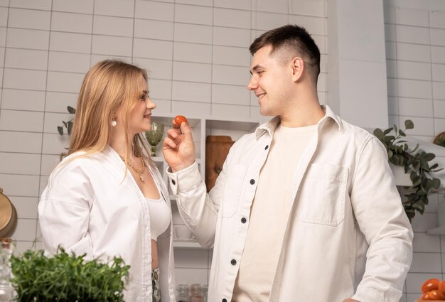 Casal feliz cozinhando juntos em casa homem alimentando namorada ou esposa enquanto faz salada de legumes frescos na cozinha branca moderna em estilo scani conceito de fim de semana de família alegre