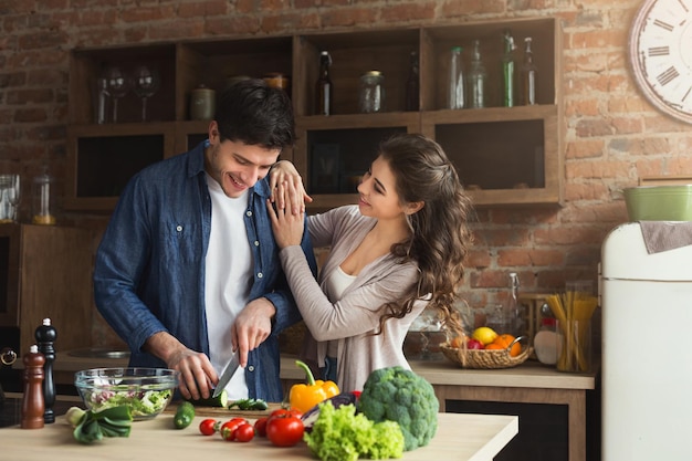 Casal feliz cozinhando o jantar juntos na cozinha do sótão em casa. Homem preparando salada de legumes para a namorada, copie o espaço