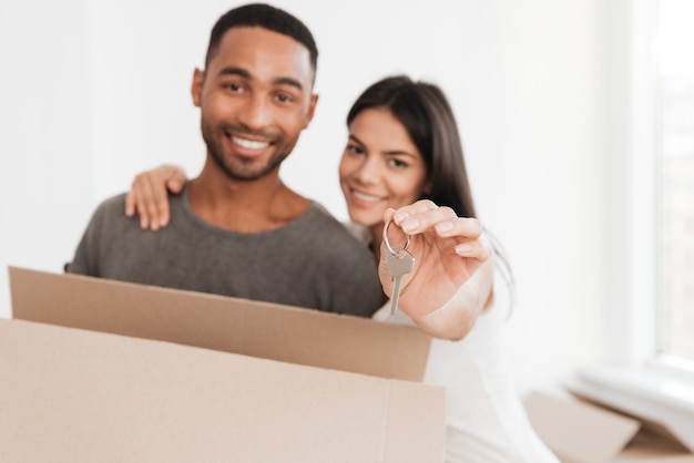 Casal feliz dançando com caixas desempacotadas. Mulher abraçando o homem. Homem segurando a caixa e a chave. Olhando para a frente. Concentre-se na chave.