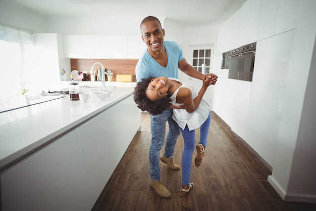 Casal feliz dançando na cozinha e olhando para a câmera