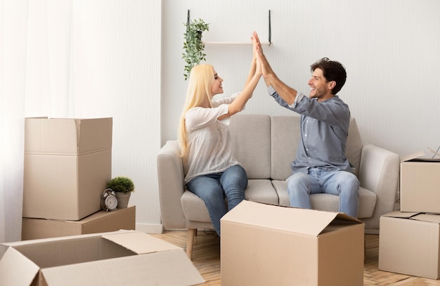 Casal feliz dando highfive sentado no sofá entre caixas em movimento