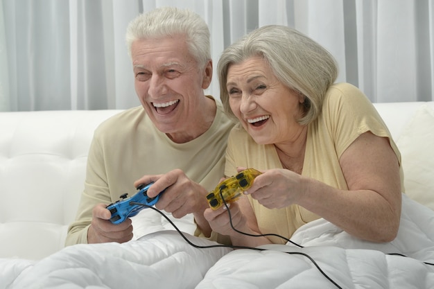 Casal feliz de idosos descansando na cama jogando videogame