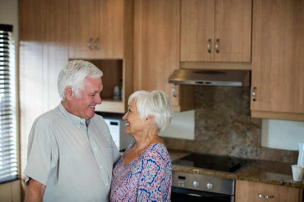 Casal feliz de idosos olhando um para o outro na cozinha de casa