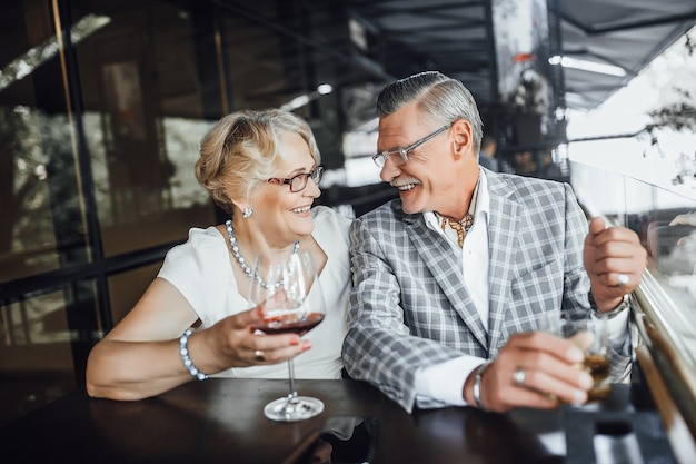 Casal feliz de idosos tilintando taças de vinho branco, comemorando aniversário