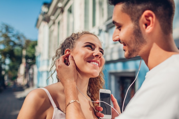 Casal feliz de raça mista apaixonado, ouvir música na cidade. Homem árabe coloca fone de ouvido no ouvido da namorada. Jovens se divertindo