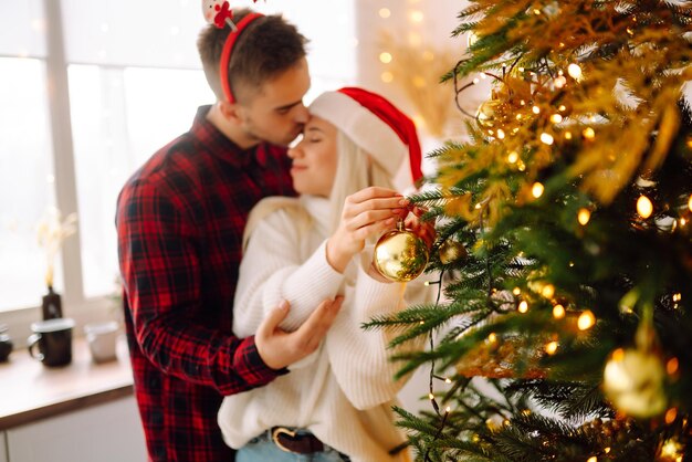 Casal feliz decorando a árvore de natal em casa sorrindo homem e mulher juntos celebrando o natal