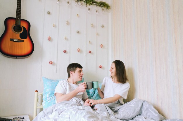 Casal feliz deitado na cama. casa aconchegante, tomando café. Jovem, mulher bonita. Estilo de vida familiar. Amor