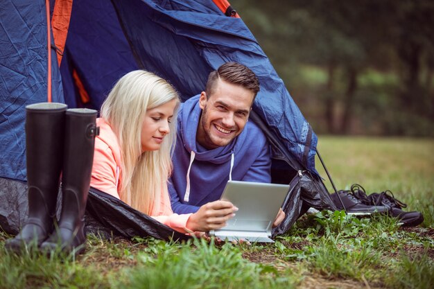 Casal feliz deitado na sua tenda usando um comprimido