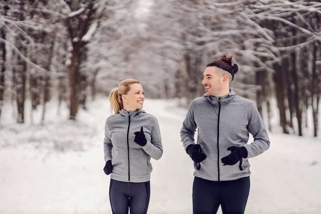 Casal feliz desportivo correndo juntos na floresta em dia de inverno nevado. União, preparação física no inverno, relacionamento