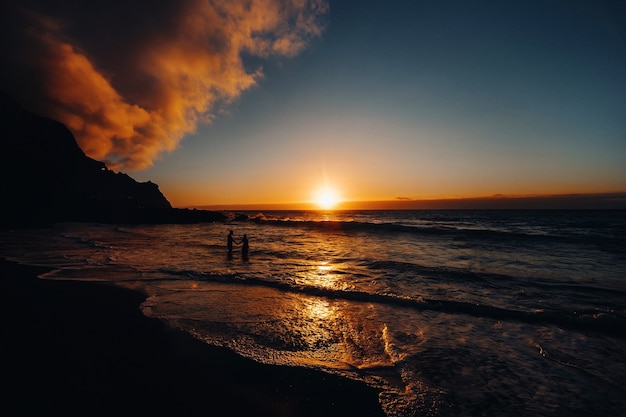 Casal feliz e alegre se divertindo correndo para o mar juntos e fazendo salpicos de água em uma praia tropical ao pôr do sol - conceito sobre férias românticas, lua de mel.