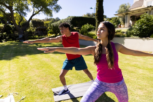 Foto casal feliz e diversificado praticando ioga em pé e alongamento no jardim ensolarado. verão, estilo de vida saudável, relaxamento e férias.