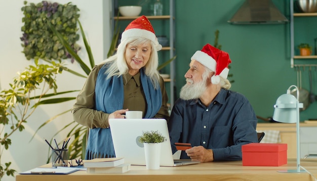 Foto casal feliz em chapéus de papai noel está escolhendo compras online de presentes de natal