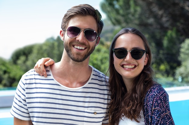 Casal feliz em óculos de sol em pé perto da piscina