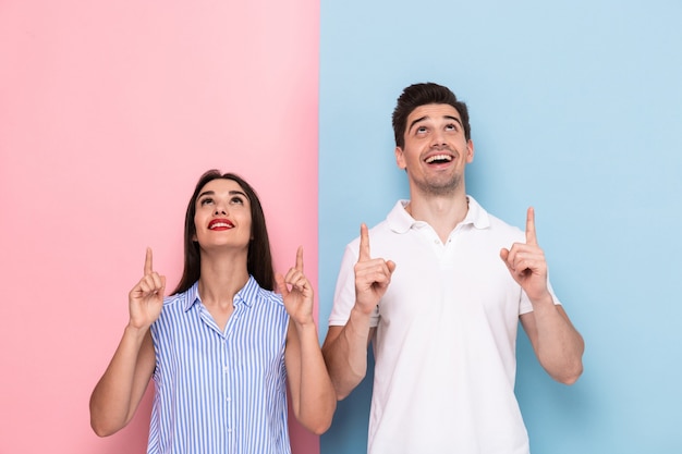 Foto casal feliz em roupas casuais sorrindo e gesticulando para cima, isolado sobre uma parede colorida