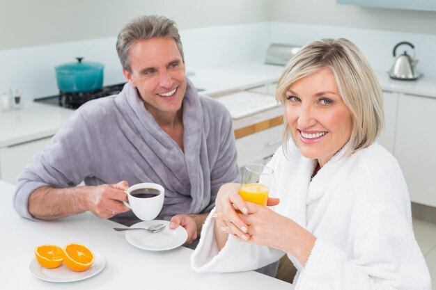 Casal feliz em roupões tomando café da manhã na cozinha