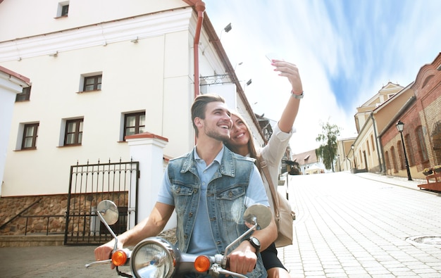 Casal feliz em scooter tirando foto de selfie em smartphone ao ar livre