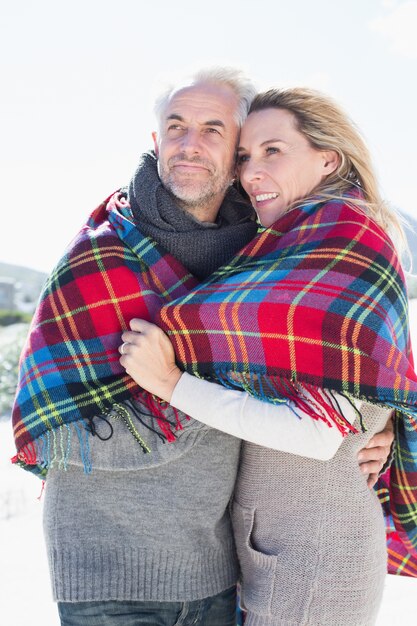 Casal feliz embrulhado em cobertor em pé na praia