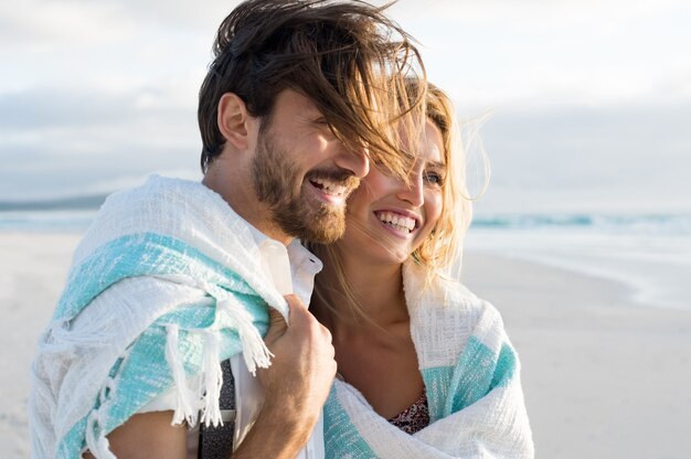 Casal feliz enrolado em cobertor na praia