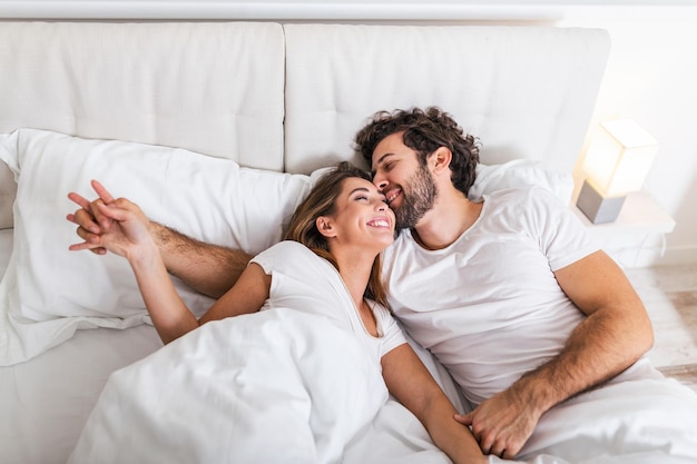 Casal feliz está deitado na cama juntos. Apreciando a companhia um do outro. Feliz casal jovem abraçando e sorrindo enquanto estava deitado na cama em um quarto em casa.