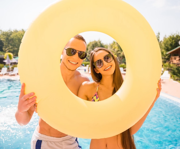 Casal feliz está posando com anel de borracha na piscina.