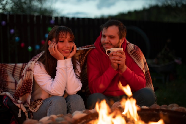 Casal feliz está relaxando perto da lareira e bebendo chá na natureza