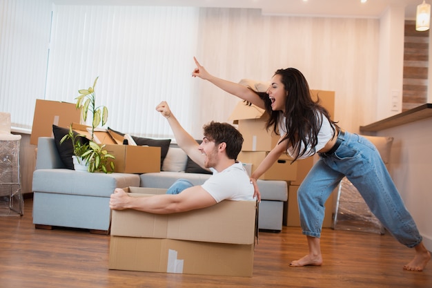 Casal feliz está se divertindo com caixas de papelão em casa nova no dia da mudança