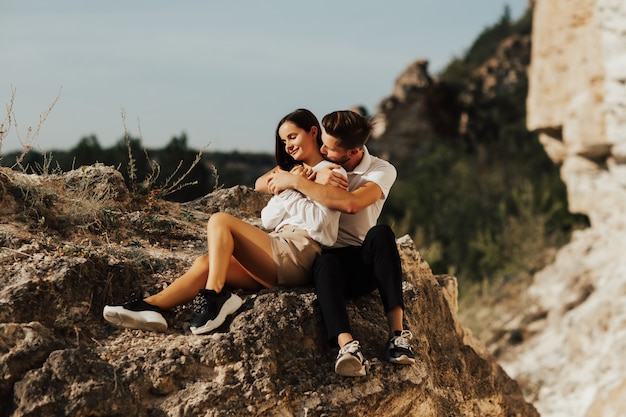 Casal feliz está sentado em uma grande pedra, enquanto aproveita o tempo juntos.