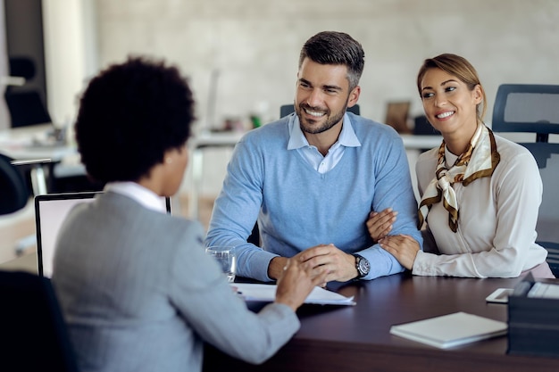 Casal feliz falando sobre termos de acordo com agente de seguros no escritório