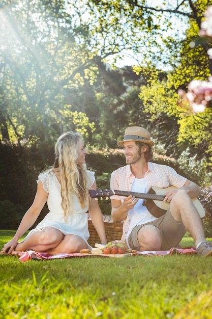 Casal feliz fazendo um piquenique e tocando violão no jardim