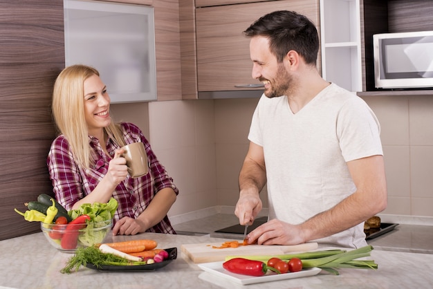 Casal feliz fazendo uma salada fresca com legumes na bancada da cozinha