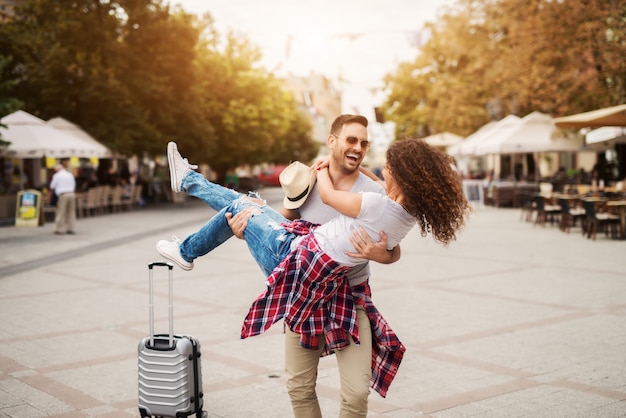 Casal feliz goza nas ruas da cidade. ele está segurando-a girando. encontre o seu parceiro de viagem.