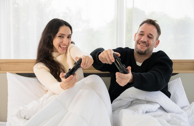 Casal feliz homem e mulher se divertindo enquanto jogam videogame juntos na cama