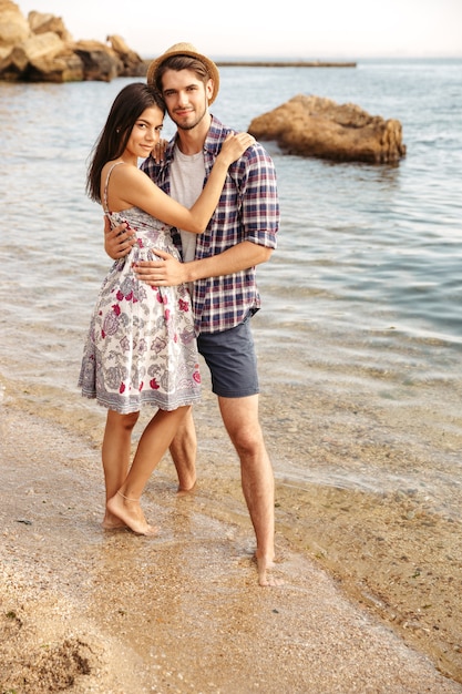 Casal feliz jovem hippie apaixonado em pé na praia e se abraçando