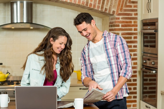 Casal feliz lendo jornal na cozinha enquanto tomando café da manhã